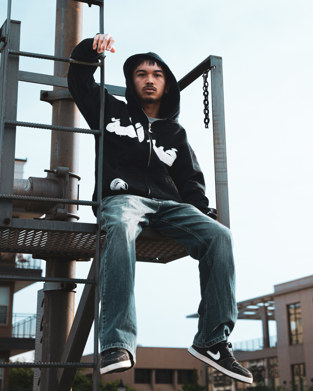 Model wearing a black MSA hoodie on a metal structure.